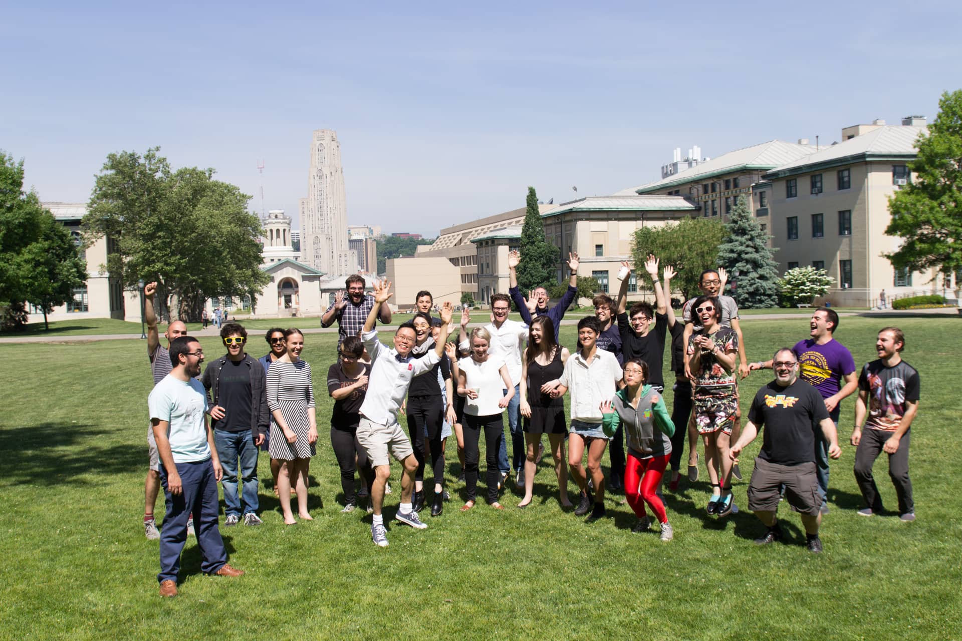 Participants jump, smile and throw their hands in the air on a green lawn"
