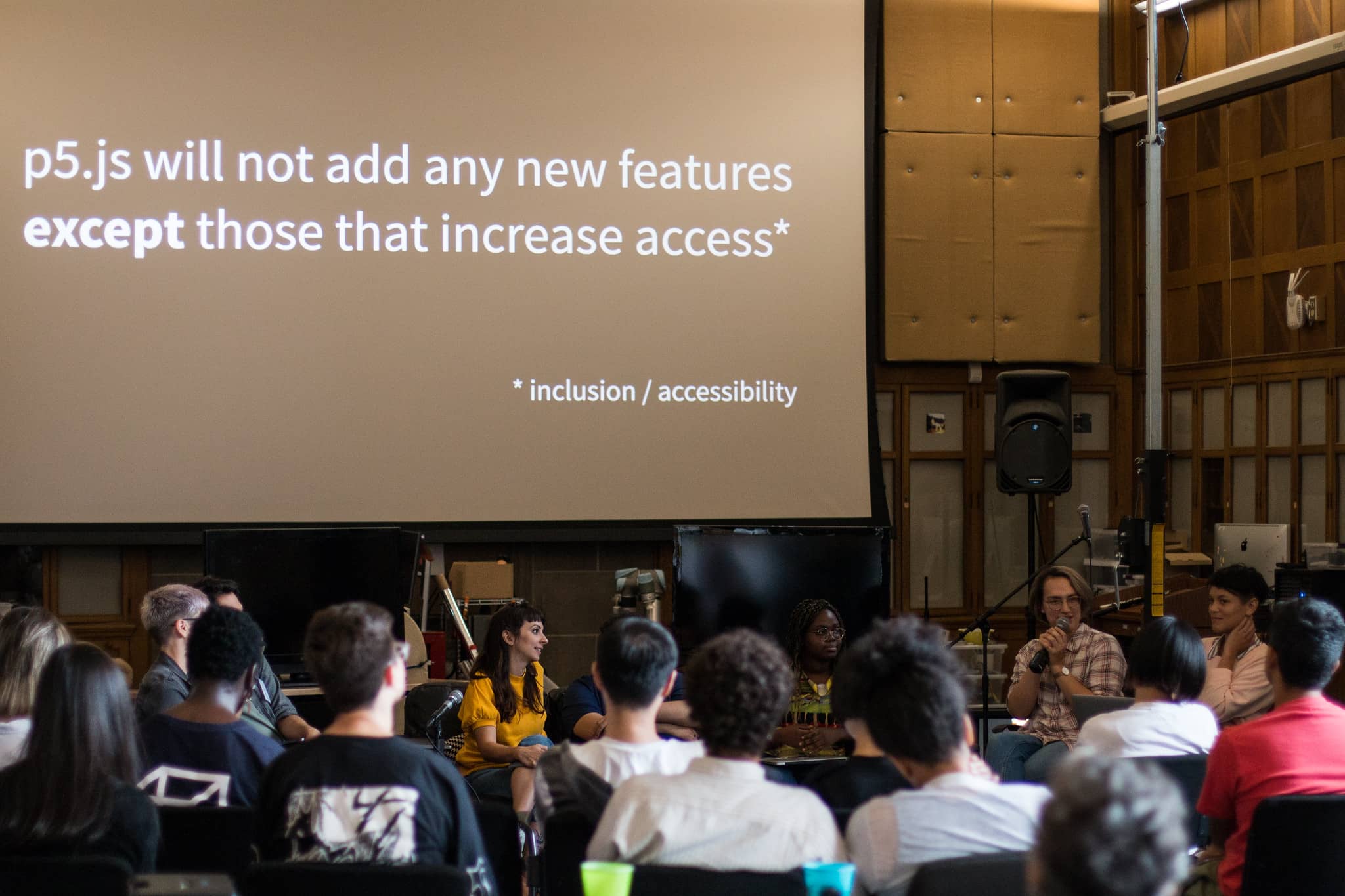 Person with a microphone speaking to fellow participants in front of text that reads p5.js will not add any new features except those that increase access"