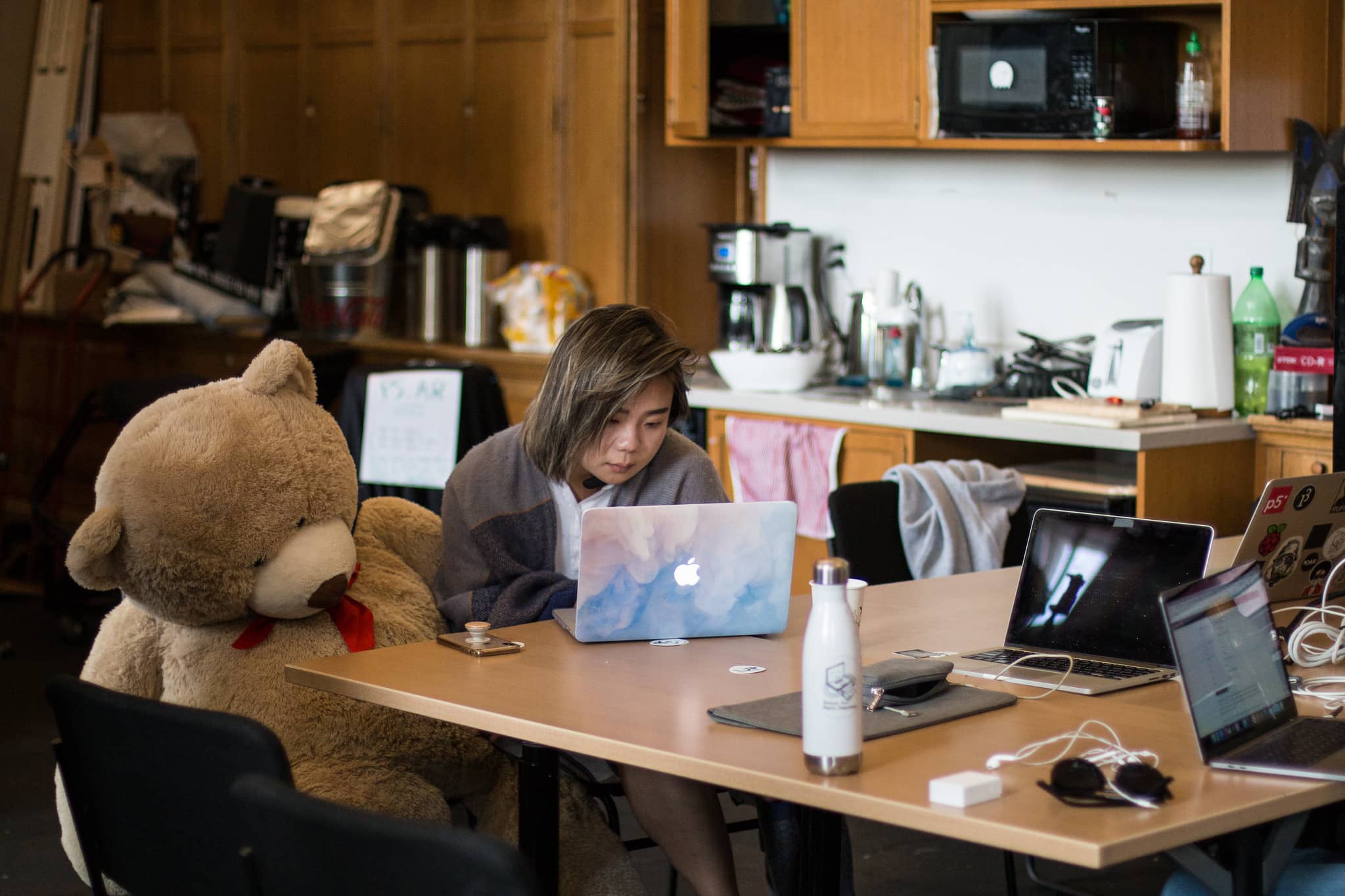 Woman sitting next to a lifesize teddy bear works on her laptop"