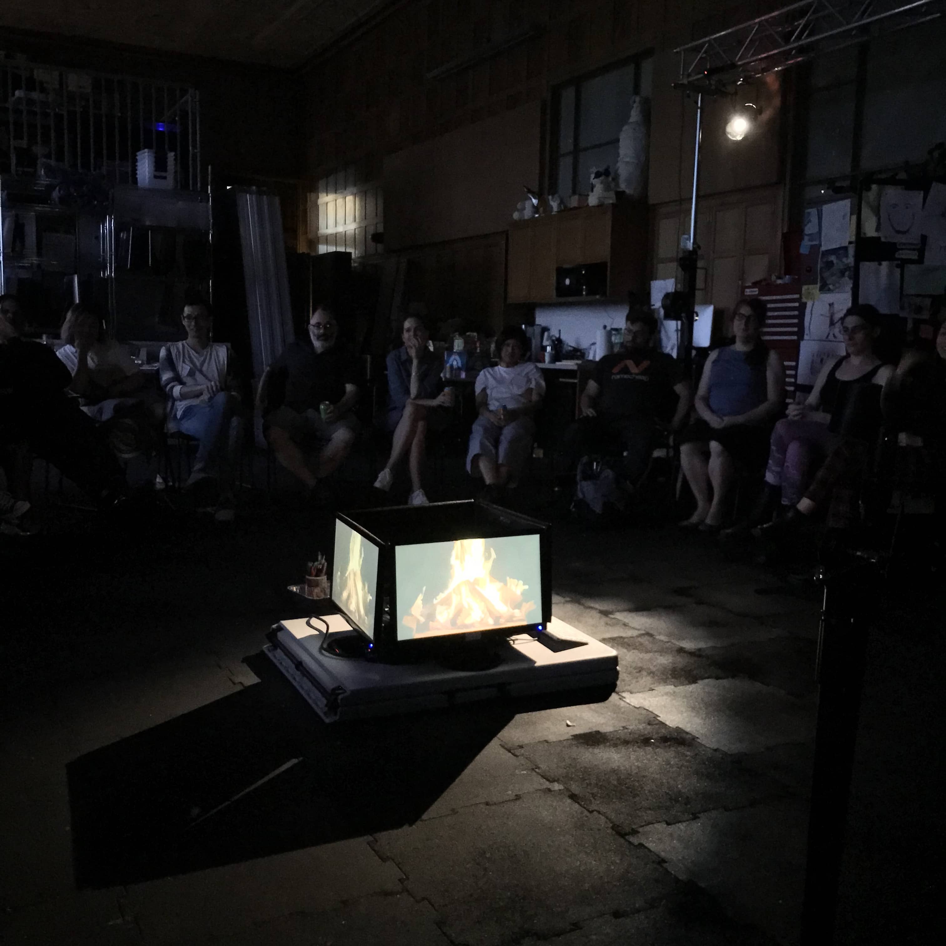 Group of people sit around campfire made from four LCD monitors."